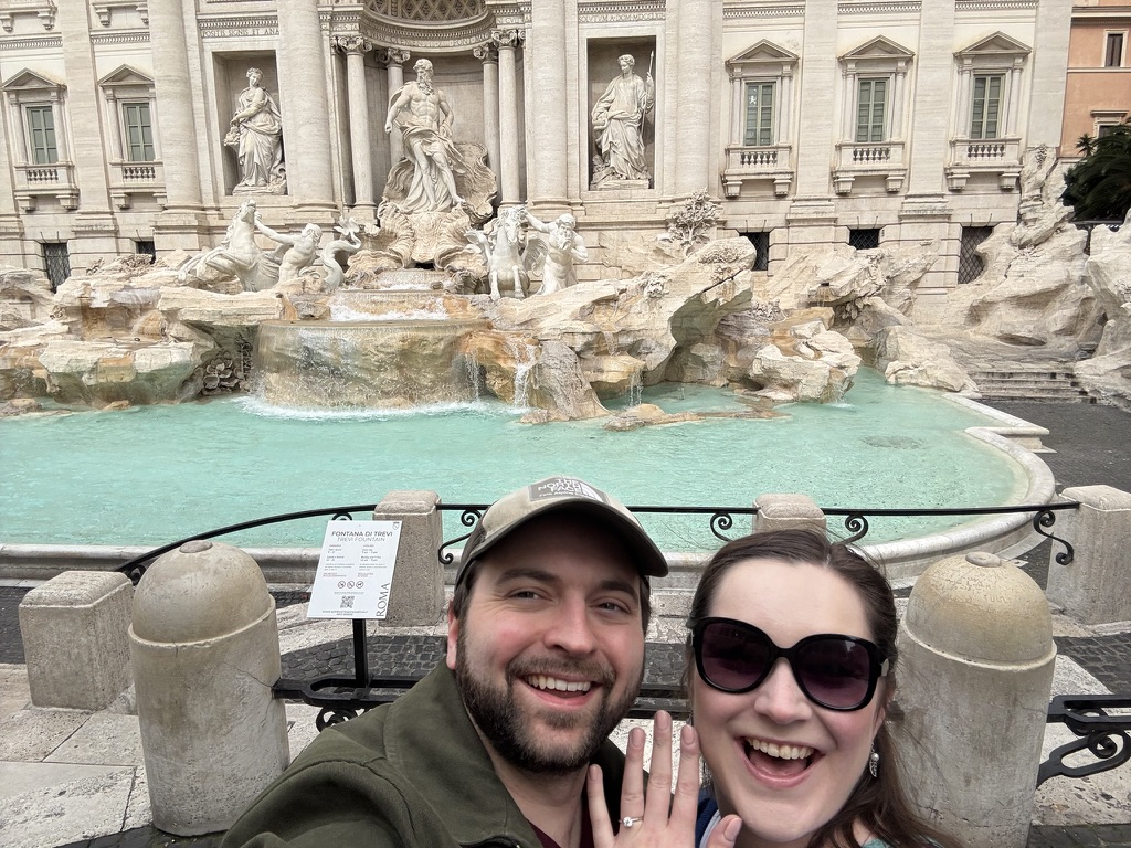 My partner and I at the Trevi Fountain in Rome. We’re both smiling, and you can see an engagement ring on her finger